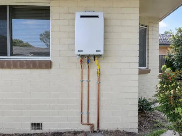 Wall-mounted hot water system with copper pipework on a cream brick exterior wall in Prairiewood